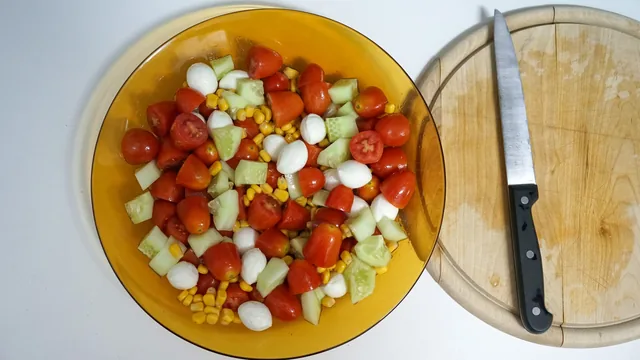 Chef's knife on a round wooden cutting board next to a bowl of chopped tomato, cucumber and mozzarella salad